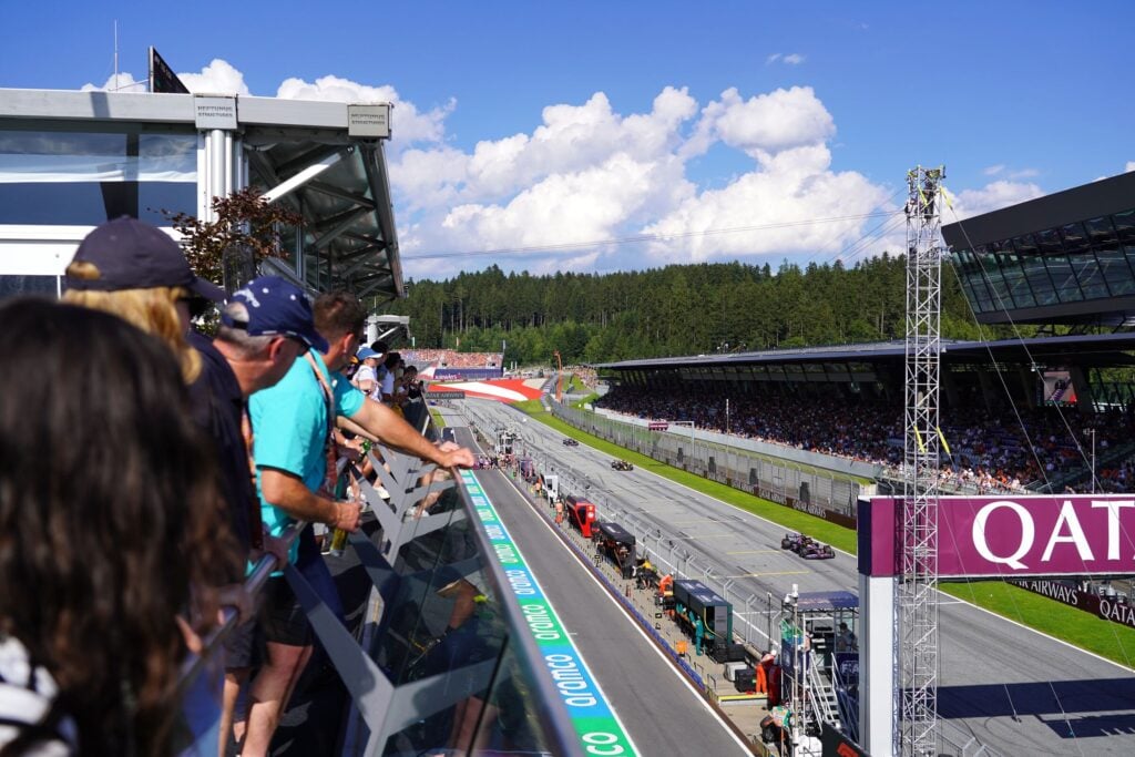 Spectators watch race at sunny motorsport circuit.