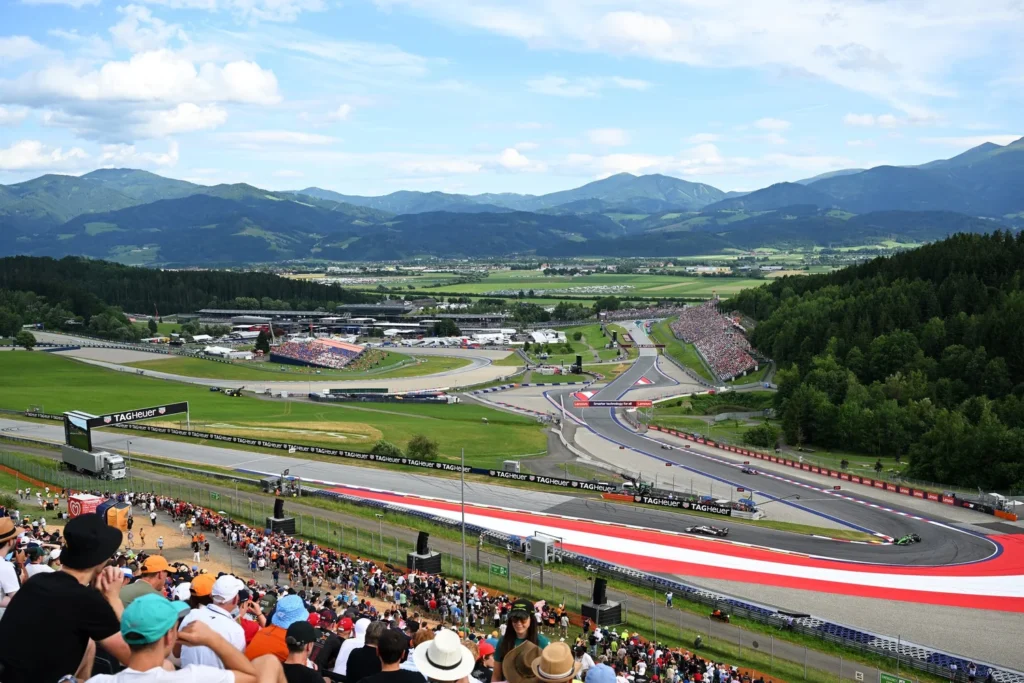 Crowded motorsport race track with mountains in background.
