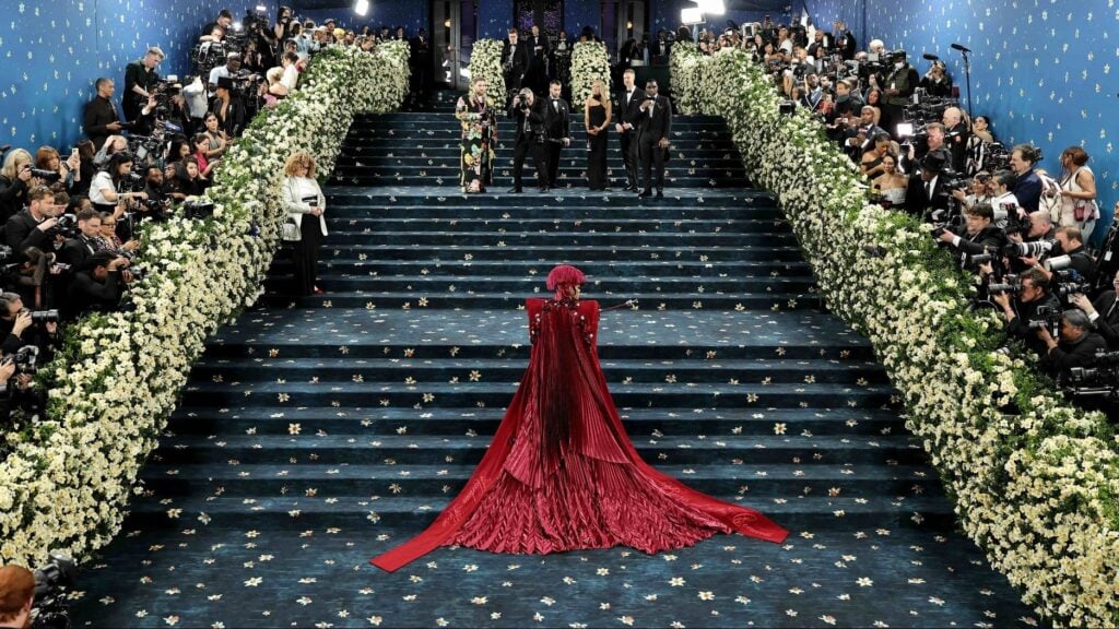 Person in red gown on flower-lined staircase.