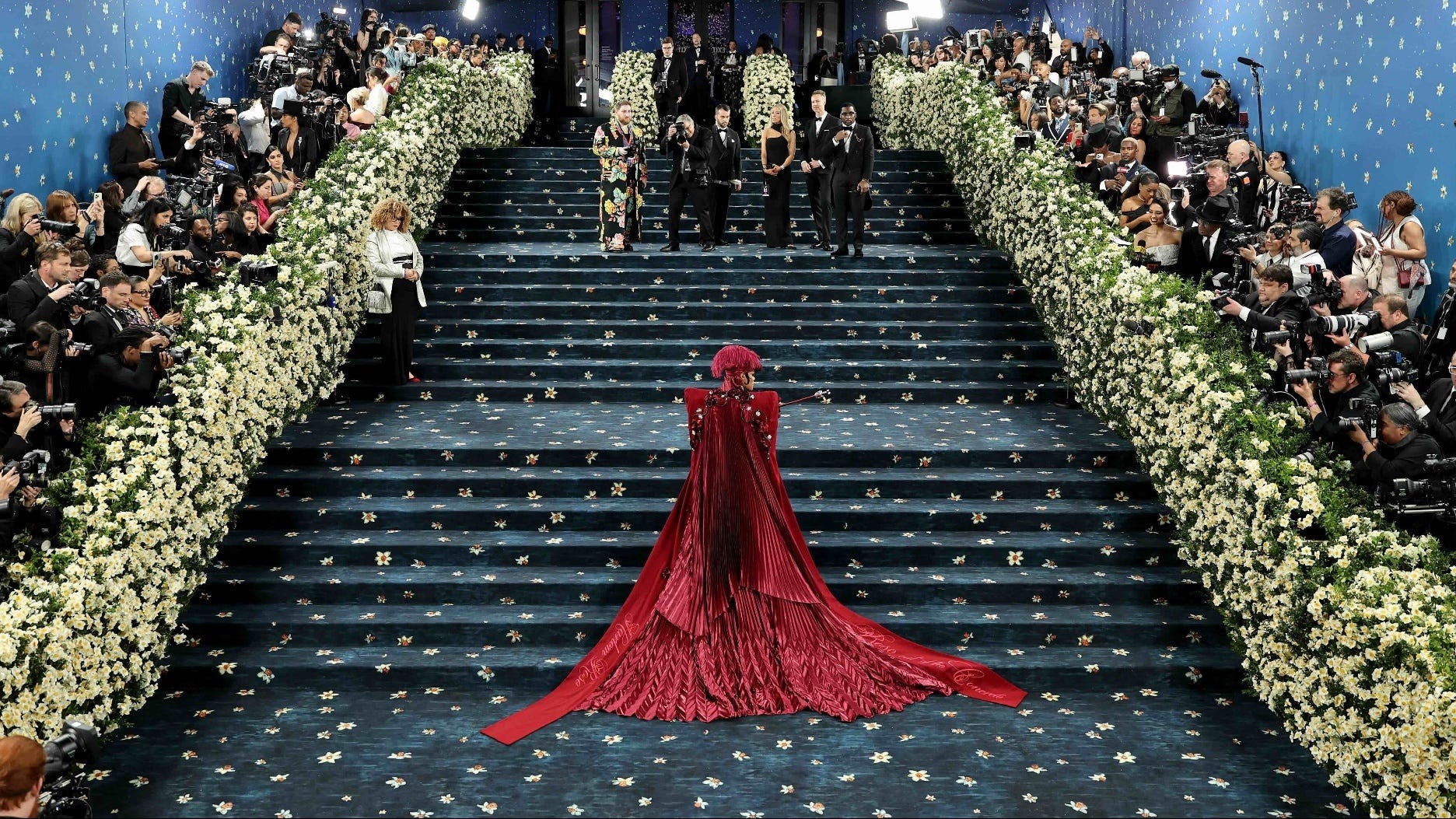 Person in red gown on flower-lined staircase.