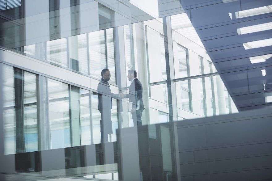Two men shaking hands in modern office building.