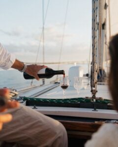 Pouring red wine on sailboat at sunset