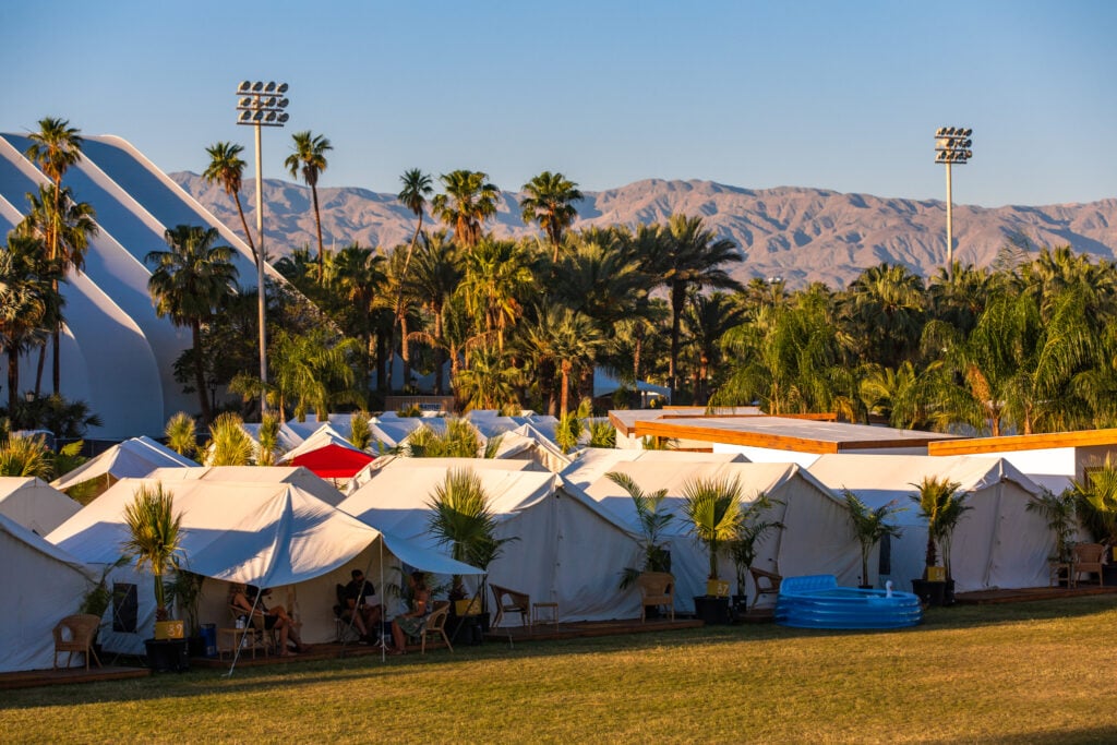 Festival tents surrounded by palm trees and mountains.