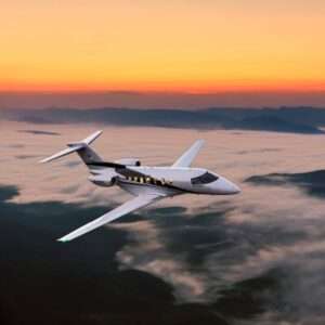 Private jet flying over mountains at sunset.