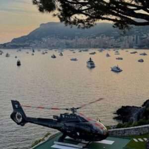 Helicopter above scenic bay with boats and cityscape.