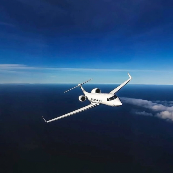 Private jet flying above ocean in clear sky.
