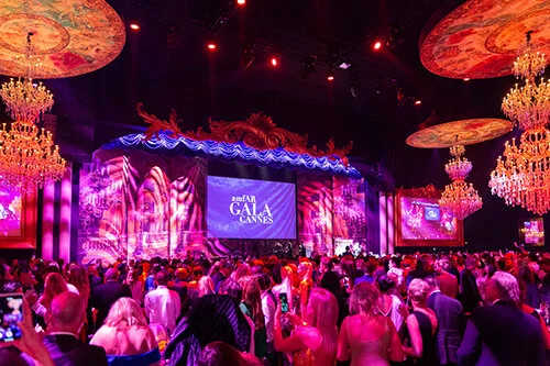 Vibrant gala event with chandeliers and crowd.