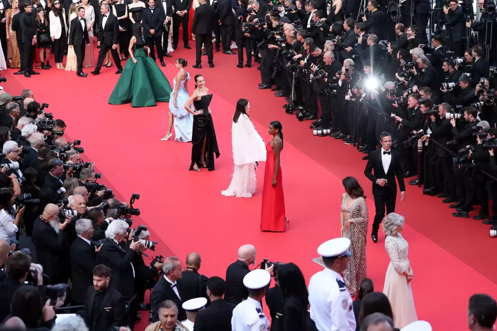 Celebrities pose on crowded red carpet event.