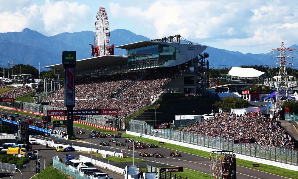 Crowded race track with mountains and ferris wheel vista.