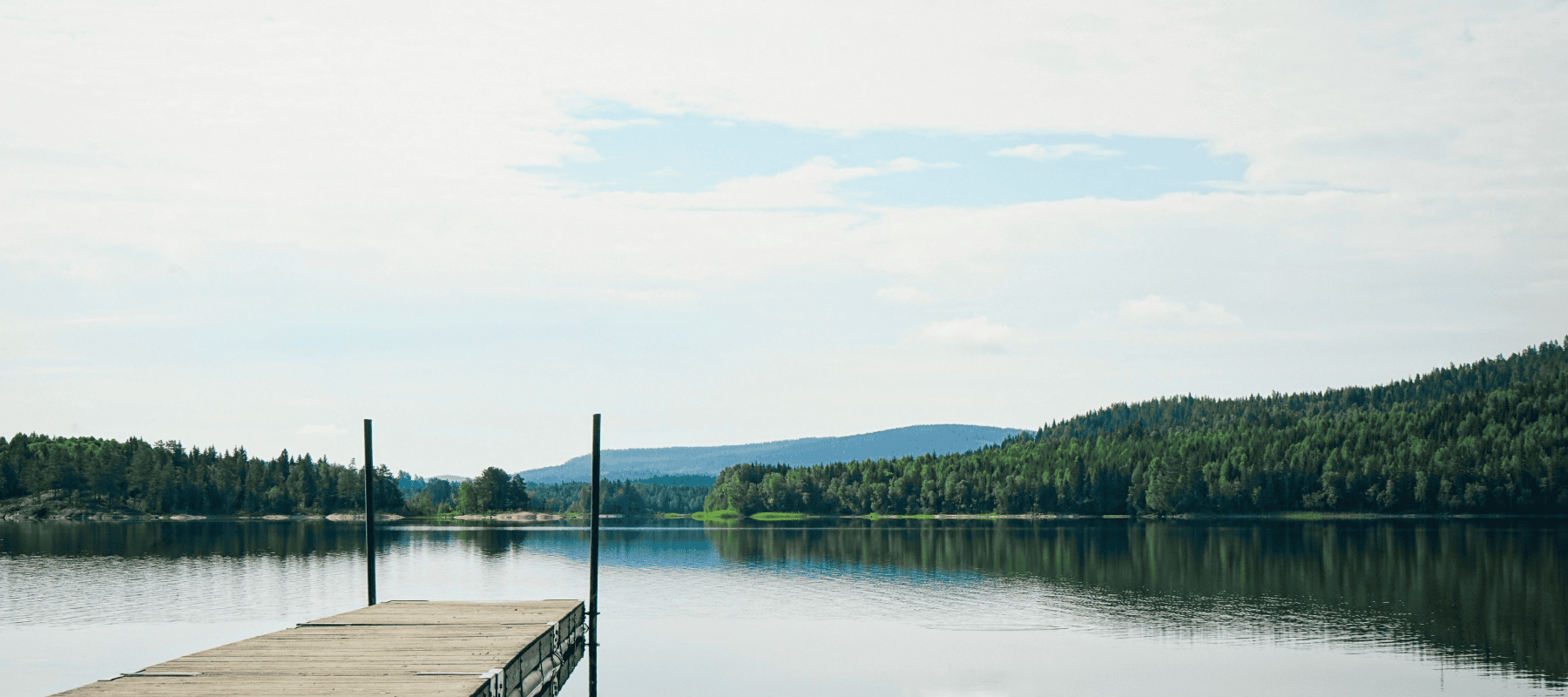 Tranquil lake with a wooden dock and forests.