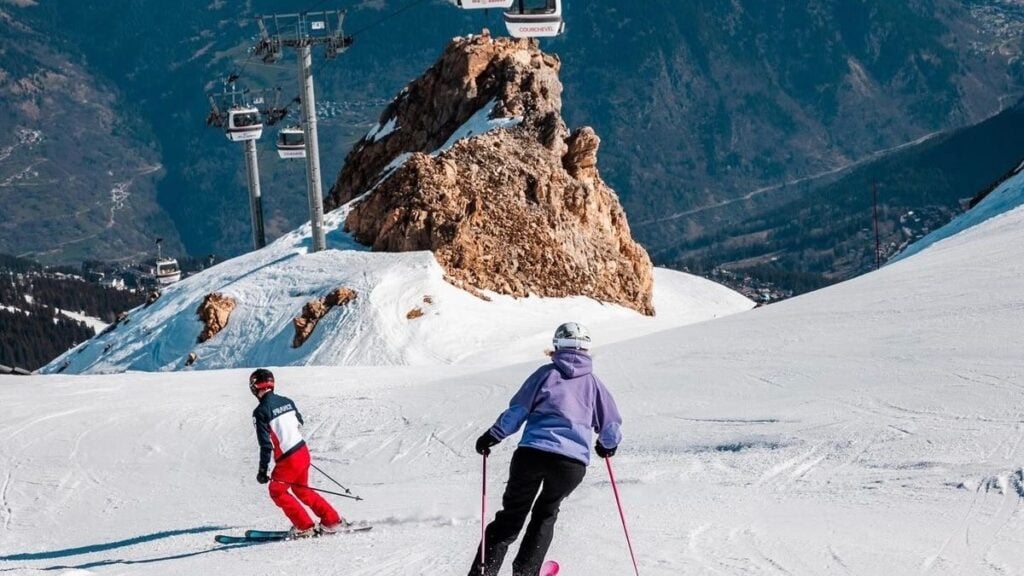 Skiers descending mountain with gondolas overhead.