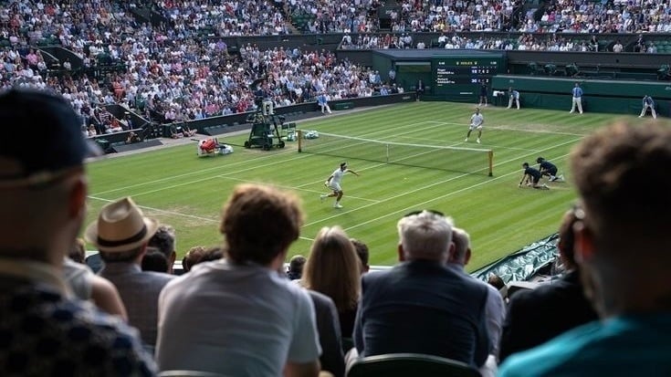 Crowd watching tennis match on grass court.