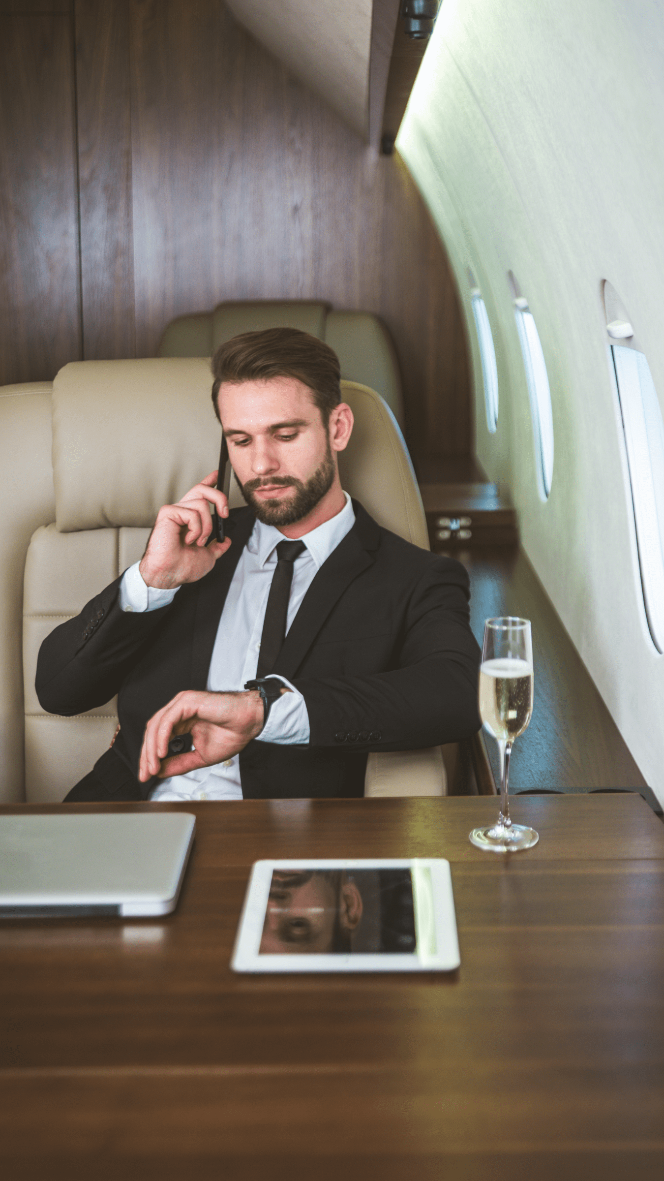 Businessman in private jet on phone, checking watch.