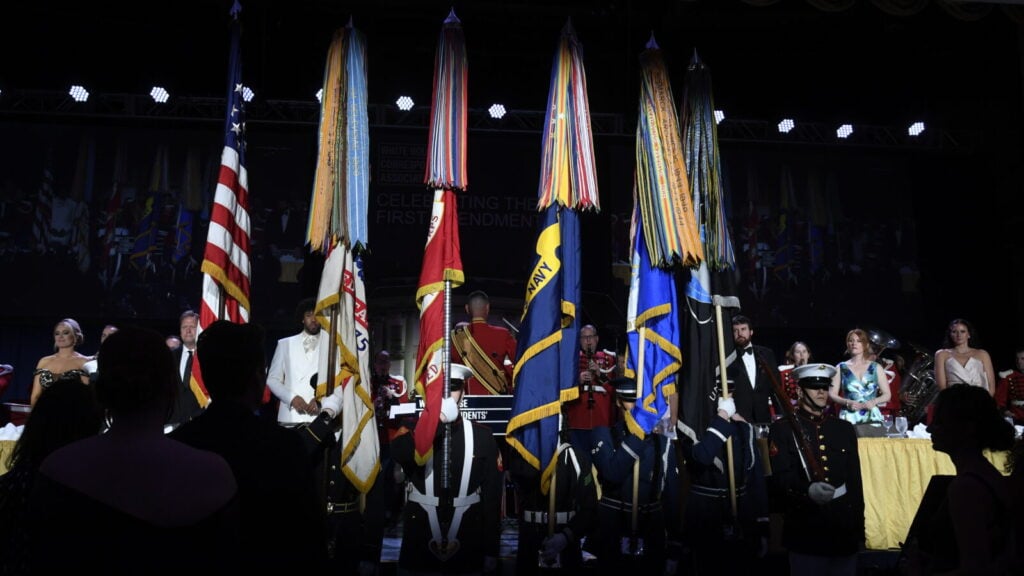 Military color guard with flags and formal event attendees.