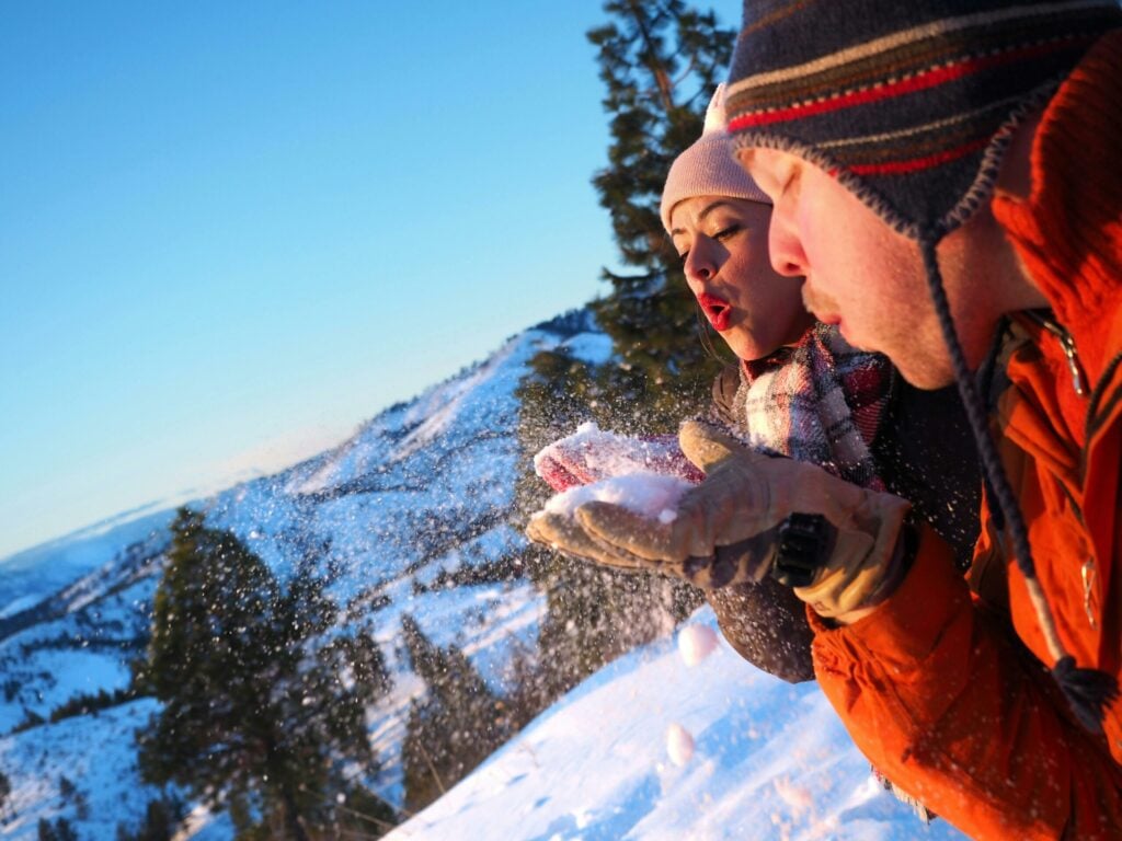 Couple blowing snow in winter landscape.