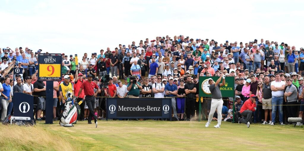 Golfer swings during tournament with large crowd.