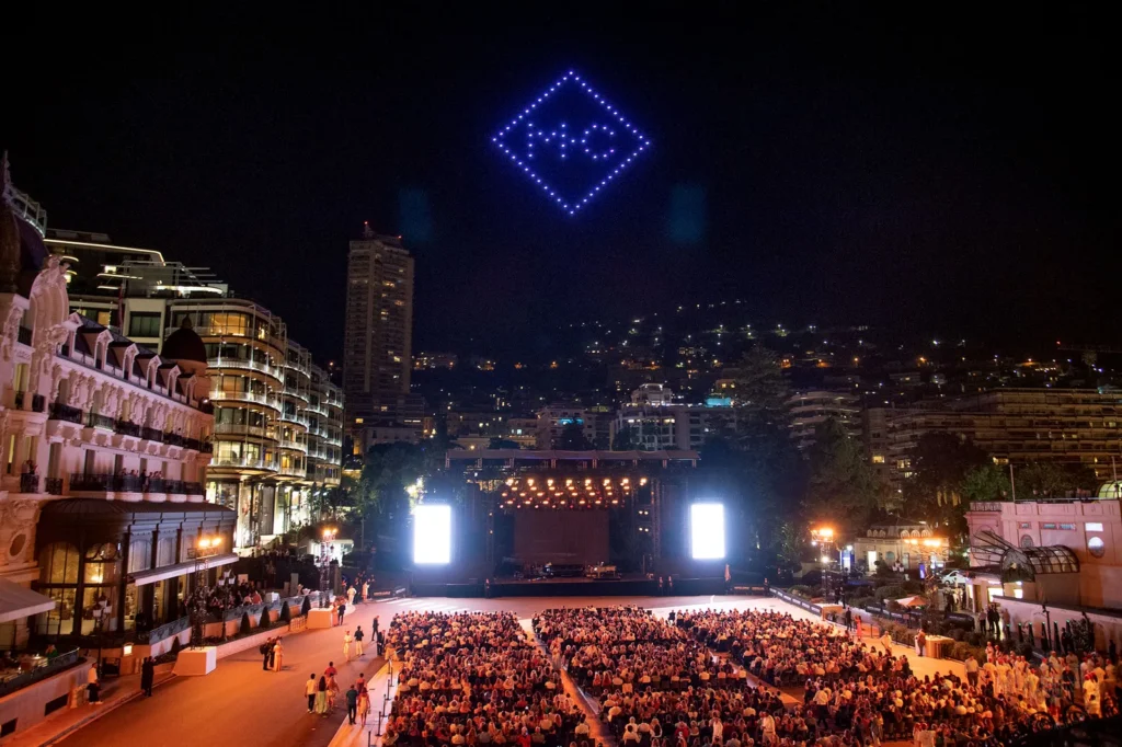 Night crowd at outdoor concert in Monaco cityscape.